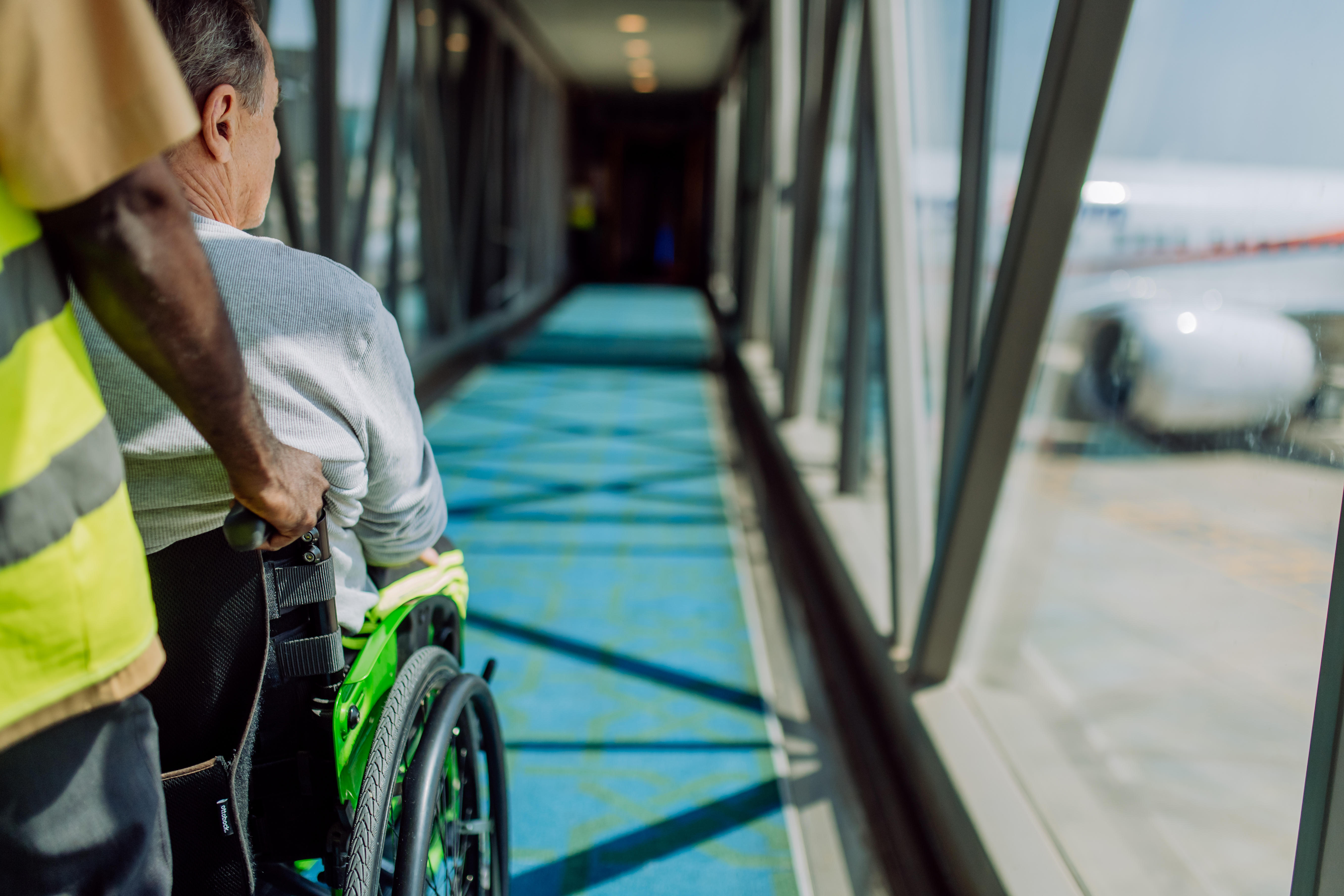 Rear view of airport worker pushing man on wheelchair in the airplane. Concept of traveling with special needs.