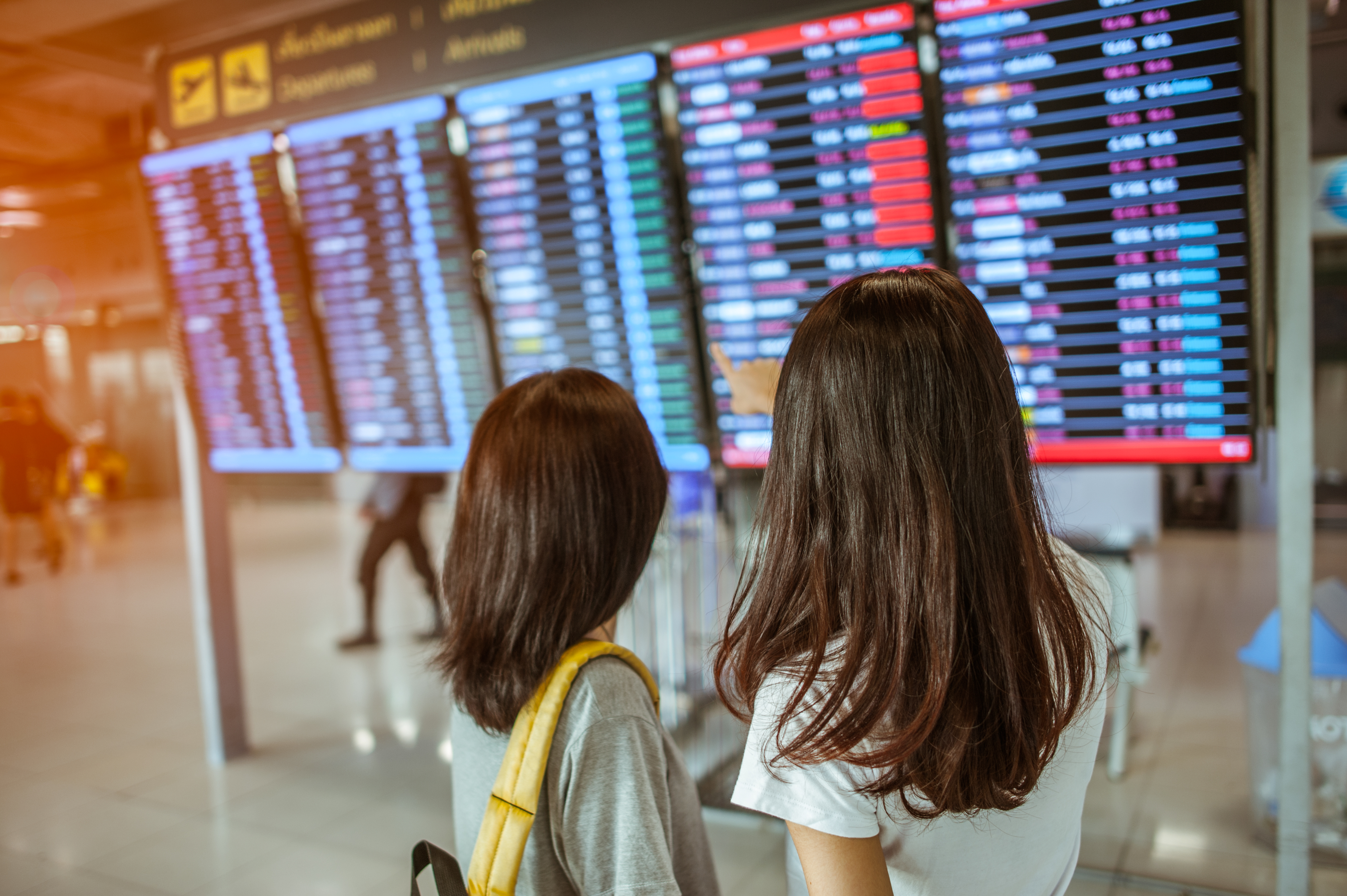 Two women in international airport terminal, looking at information board, checking her flight.